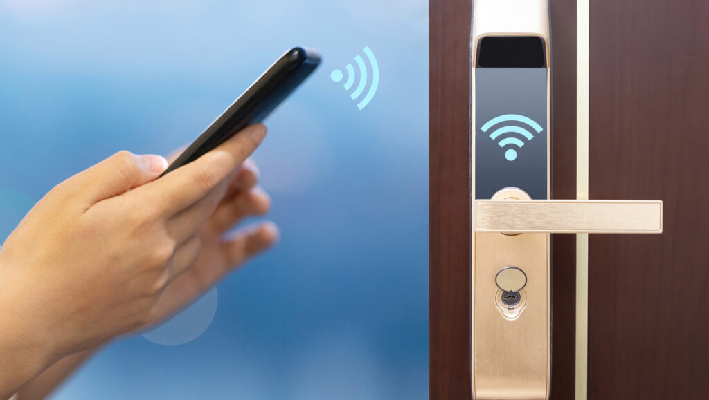 Serrure connectée : Sécurisez et facilitez l'accès à votre location Airbnb à Tanger 3 Gros plan sur une serrure connectée moderne installée sur une porte en bois, avec un smartphone affichant l'application de contrôle à proximité.